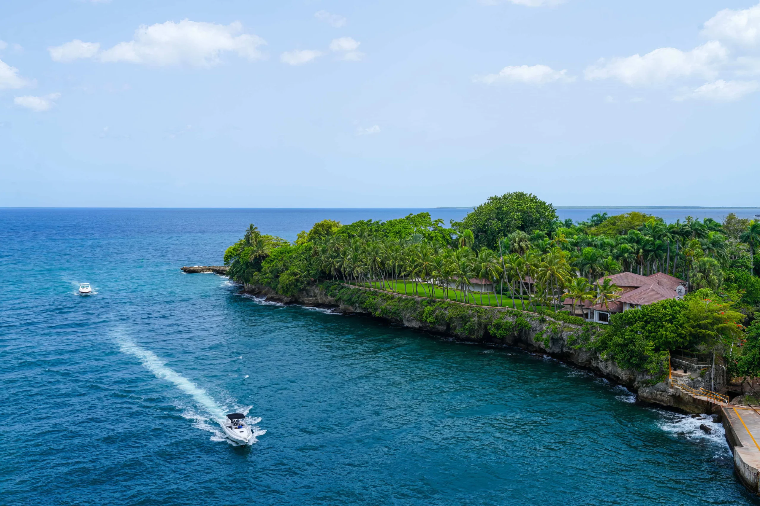 Aerial view of a tropical island coastline with boats navigating azure waters and lush greenery.